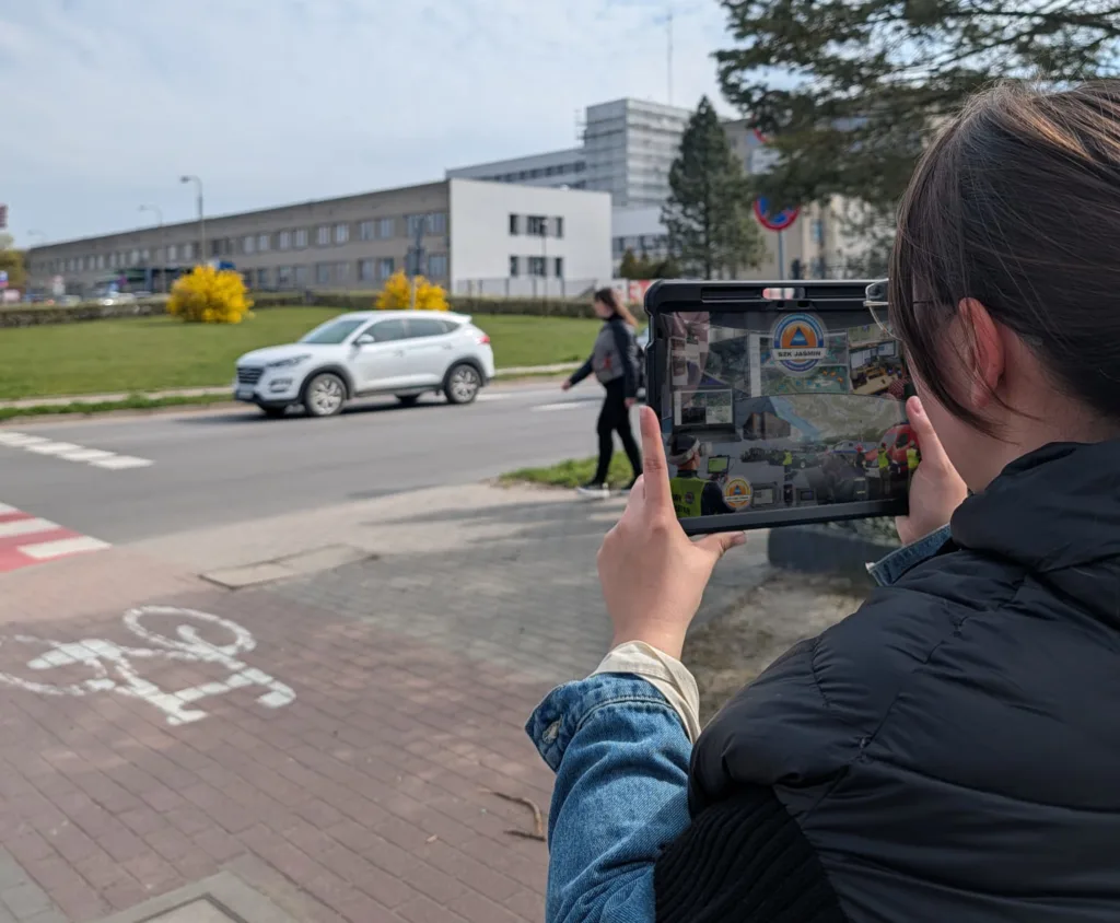 Kobieta testująca aplikację mobilną systemu JAŚMIN na tablecie przy skrzyżowaniu z drogą rowerową i przejściem dla pieszych