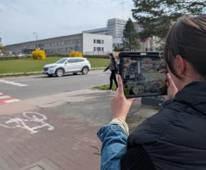 Kobieta testująca aplikację mobilną systemu JAŚMIN na tablecie przy skrzyżowaniu z drogą rowerową i przejściem dla pieszych